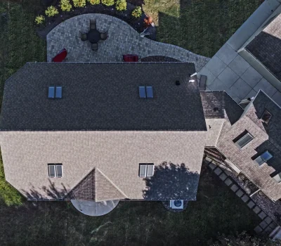 Aerial view of a house with a paved patio, seating area, and grassy yard. Adjacent buildings are partially visible.