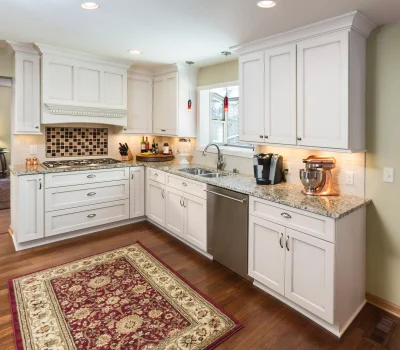 Modern kitchen with white cabinets, granite countertops, a rug, and stainless steel appliances. Warm lighting highlights the elegant, clean design.