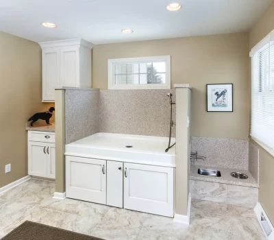 Modern pet washroom with a large tub, cabinets, and decorative dog silhouette. Neutral colors and clean design create a functional space.