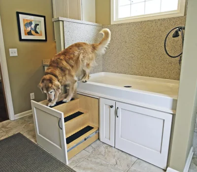 A dog descends custom pull-out stairs from a raised sink in a modern bathroom with a colorful framed artwork on the wall.