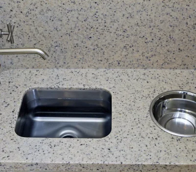 A modern, speckled granite countertop with a stainless steel faucet and two integrated sinks, one rectangular and one circular. Minimalist design.