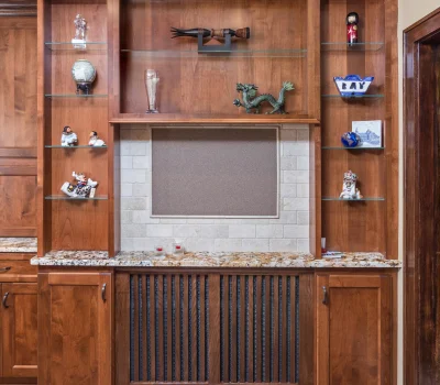 A wooden display cabinet with glass shelves features various figurines, a dragon sculpture, and decorative pottery. Marble countertop and brick backsplash.