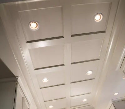 Elegant kitchen ceiling with recessed lighting and coffered design. Cabinets and pendant lights underlining sophisticated architectural features in a modern home interior.