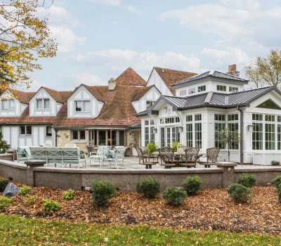 A charming Tudor-style house with a spacious patio, surrounded by autumn foliage. Elegant outdoor seating complements the scenic, tranquil setting.