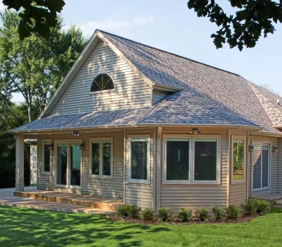 A cozy suburban house with a sloped roof, surrounded by lush green grass and trees, on a sunny day. No people visible.