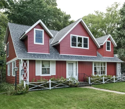 A charming red house with white trim, surrounded by lush greenery and a well-maintained lawn, under a cloudy sky.