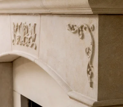 Intricately carved stone fireplace detail with decorative floral motifs, showcasing elegant craftsmanship and classical design elements in a neutral beige tone.