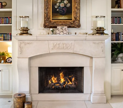 Elegant fireplace with intricate carvings, flanked by bookshelves. Above, a classic painting in a decorative frame. Cozy ambiance with firewood flames.