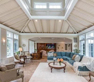 Spacious living room with vaulted ceiling, blue sectional sofa, large windows, elegant furniture, an aquarium, and a cozy seating area. Bright and inviting.