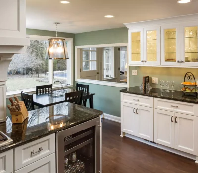 Modern kitchen with dark countertops, white cabinets, and a dining area. Large windows offer a view of the backyard and pool.