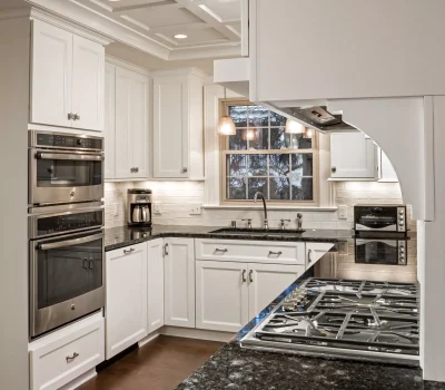 Modern kitchen with white cabinets, black granite countertops, stainless steel appliances, gas stove, and a window view. Elegant coffered ceiling enhances the design.