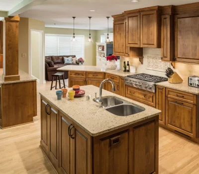 A spacious kitchen with granite countertops, wooden cabinetry, pendant lighting, and stainless appliances. Cozy living area with a brown sofa in the background.