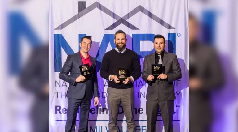 Three people holding awards stand in front of a NARI banner at an event. They are smiling and dressed in formal attire.