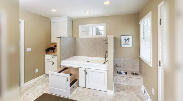 A pet washing station with a shower, brown walls, and white cabinets. Dog silhouette decoration on the counter. Bright, natural light.