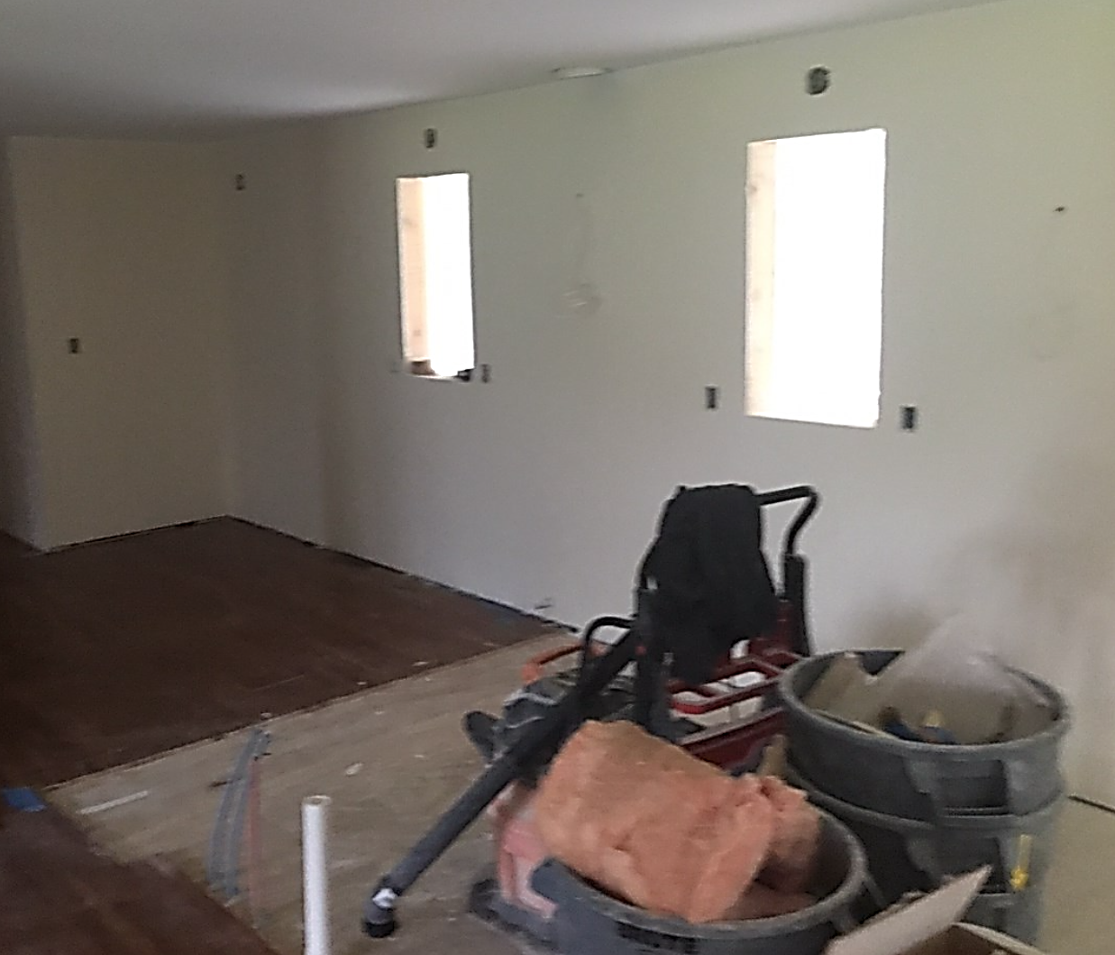 A partially renovated room with unfinished walls, construction materials, insulation, and tools scattered around the floor, indicating ongoing work.