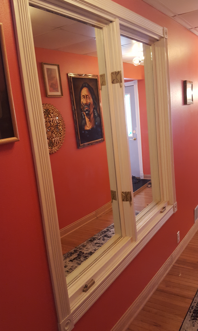A mirror reflects a hallway with red walls, wooden floor, and artwork featuring a person. Warm lighting creates a cozy atmosphere.